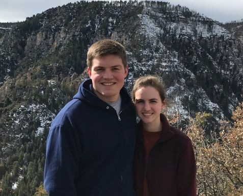 Two friends standing side by side on a snowy mountainside, smiling at the camera.